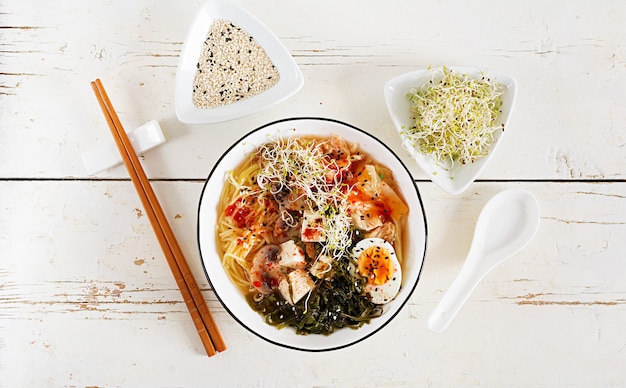 Miso noodles with cabbage kimchi, seaweed, egg, mushrooms and cheese tofu in bowl on white wooden table