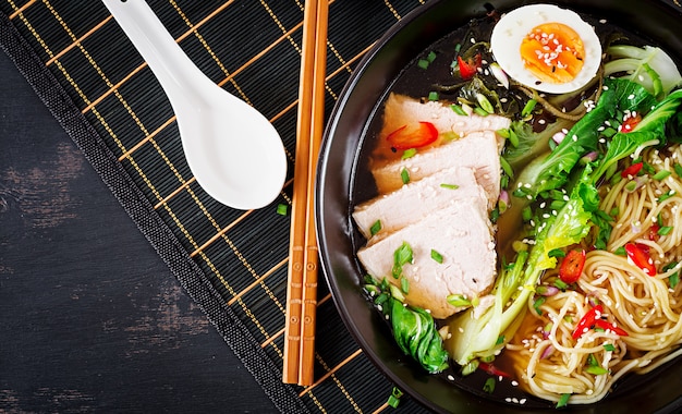 Miso noodles with egg, pork and pak choi cabbage in bowl on dark table