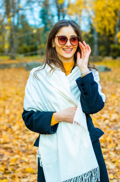 Miss gekleed in een jas met bril op de achtergrond van herfstbladeren