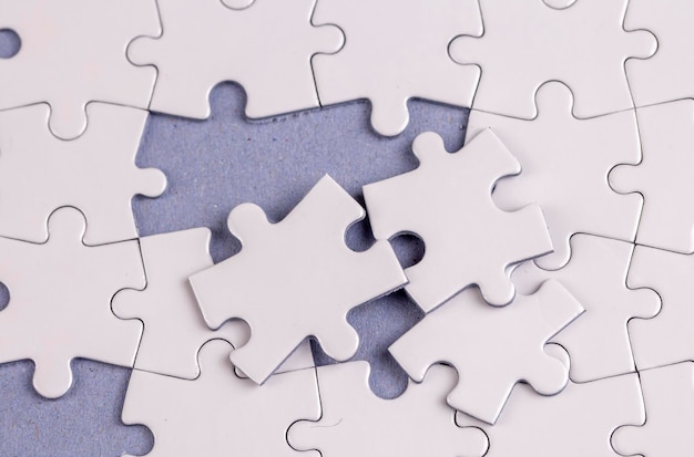 Missing jigsaw puzzle pieces. Business concept. Fragment of a folded white jigsaw puzzle and a pile of uncombed puzzle elements against