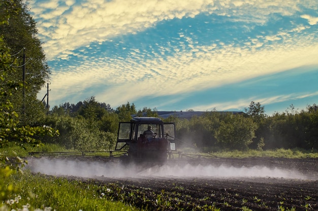Облако тумана за сельскохозяйственным трактором, который применяет гербициды на картофельное поле