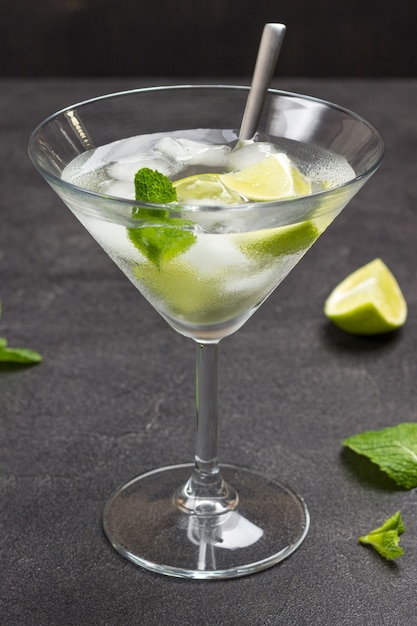 Misted wine glass with lime and ice. Mint sprigs on table. Black background. Top view