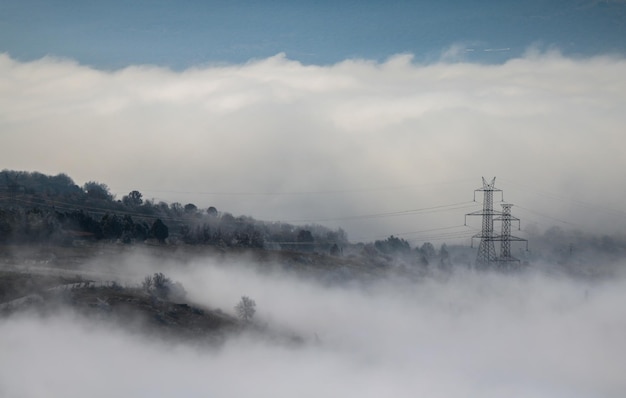 Mistige bergen voor achtergrond Elektrische pyloon tussen mist en wolken Bos in de winter