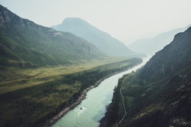 Misty mountain landscape with wide mountain river. Dark green gloomy scenery with confluence of two mountain river in mist. Dark atmospheric view to confluence of great rivers in rainy weather.