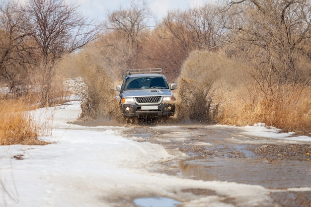 Mitsubishi Pajero Sport on dirt road in early spring making splashes from a puddle