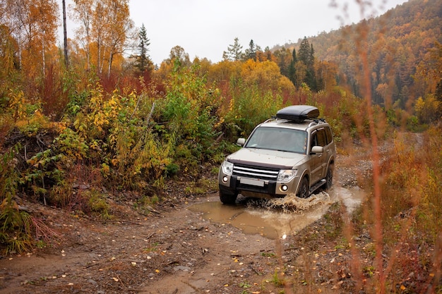 Mitsubishi Pajero steekt een plas over op een onverharde bosweg in de herfst