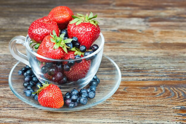 Mix of berries in a a transparent cup on brown wooden background. strawberry, blueberry