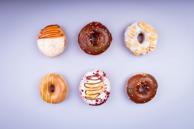 Mix of delicious colorful glazed donuts on purple background - top view