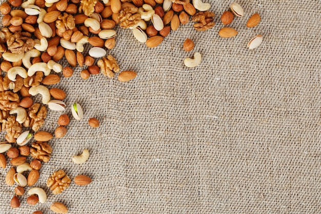 Mix of different nuts in a wooden cup against the  of fabric from burlap. Nuts as structure and background, macro. Top view.