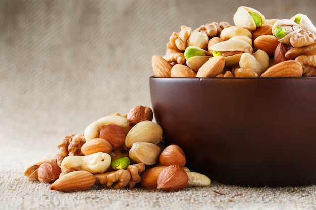 Mix of different nuts in a wooden cup against the  of fabric from burlap. Nuts as structure and background, macro. Top view.