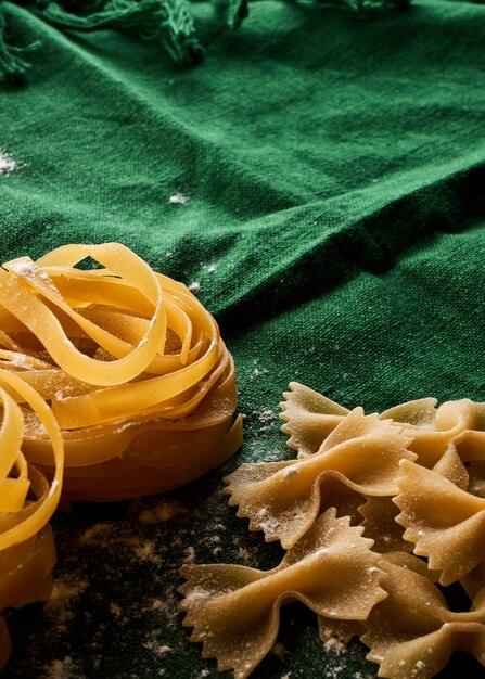 Mix of different varieties of pasta on green fabric background, cooking assorted macaroni concept