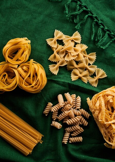 Mix of different varieties of pasta on green fabric background, cooking assorted macaroni concept