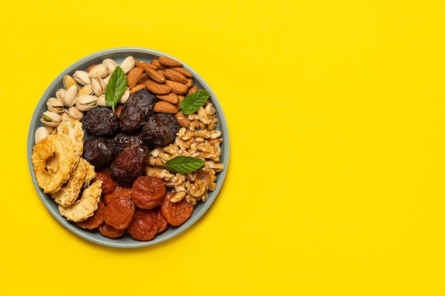 Mix of dried fruit and nuts on a plate on yellow background with copy space. View from above. Symbols of the Jewish holiday of Tu Bishvat