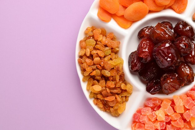 Mix of dried fruits and nuts on a white plate. Apricot, almond, raisin, dates fruit. On a lilac background. Space for text or design.