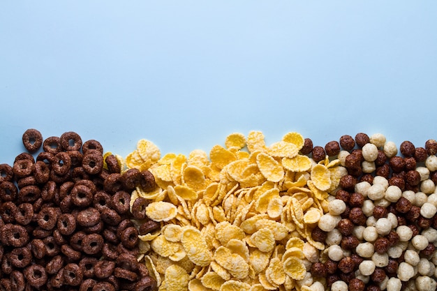 Foto mix di palline secche, di cioccolato, anelli e corn flakes gialli per cereali colazione su sfondo blu