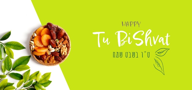 Mix of dry fruits and nuts in a wicker plate branch with young green leaves Concept of the Jewish holiday Banner with the inscription Tu Bishvat in English and Hebrew