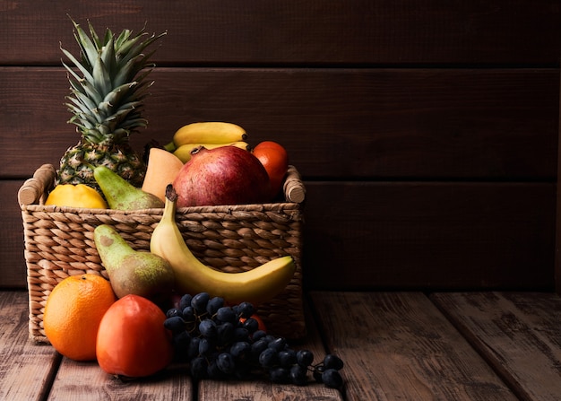 Mix of fresh juicy colorful exotic tropical fruits in basket on wooden background