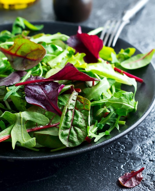 Mix fresh leaves of arugula, lettuce, spinach, beets for salad on a dark stone background. Selective focus.