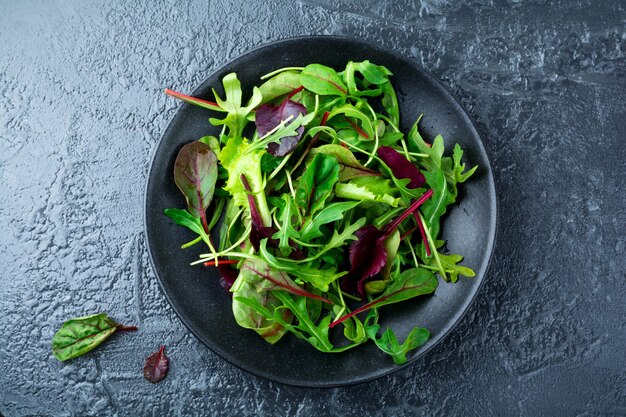 arugula, 양상추, 시금치, 샐러드 용 사탕무의 신선한 잎을 어두운 돌 표면에 섞으십시오.