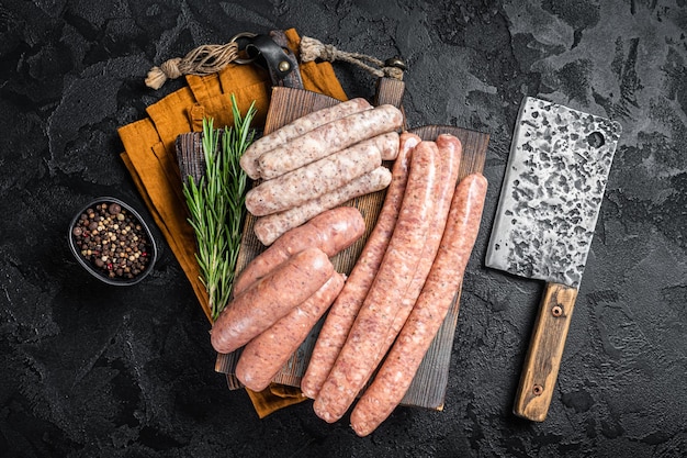 Mix fresh raw sausages Beef pork lamb and chicken mince meat sausages on a butcher cutting board with spices Black background Top view