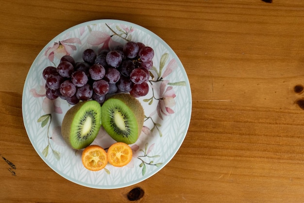 Foto mix di frutta uva kiwi e arancia divisa a metà servita su un piatto di porcellana bianca