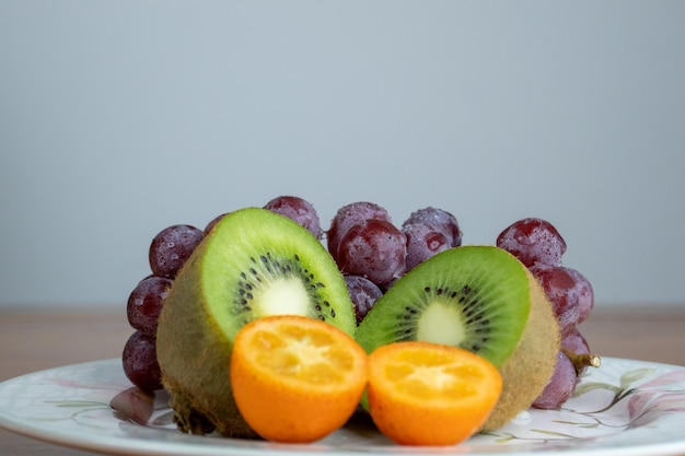 mix of fruits grapes kiwi and orange divided in half served on a white porcelain plate