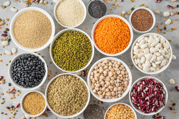 Mix of legumes, chickpeas, lentils, beans, peas, quinoa, sesame, chia, flax seeds in bowls on a gray concrete background. Healthy, vegan and gluten free food. Top view.