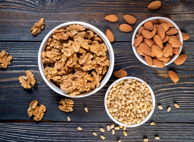 Mix nuts in white bowl on wooden dark background, mix of walnuts, almonds and cedar