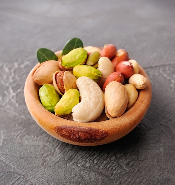 Mix of nuts in wooden plate on concrete table. Peanut, cashew, pistchios