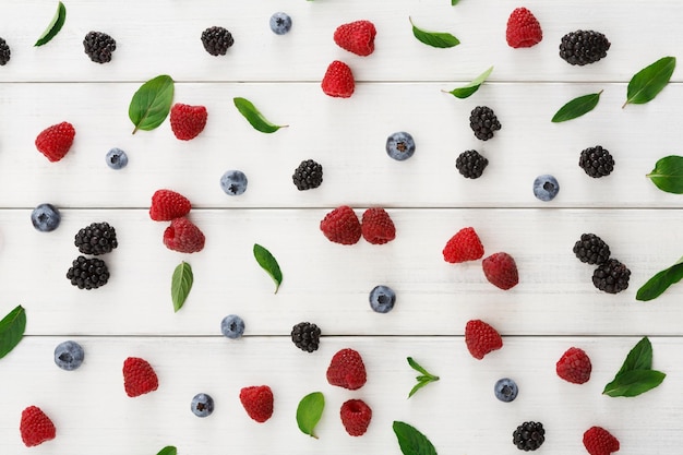 Mix of organic berries background. Pattern of fresh raspberries, blueberries, blackberries and mint leaves on white wooden table, top view