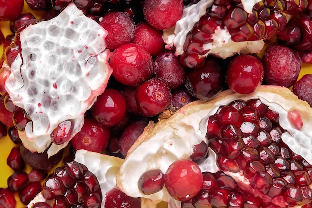 A mix of pomegranate seeds and frozen cranberries on a yellow background. Suitable for advertising juice, smoothie recipes. The concept of healthy eating.