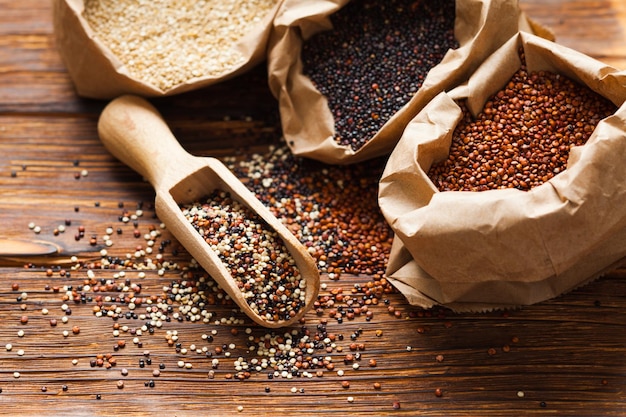 Mix of quinoa seeds in the wooden scoop. White, red and black quinoa in paper bags on the table, healthy lifestyle food concept