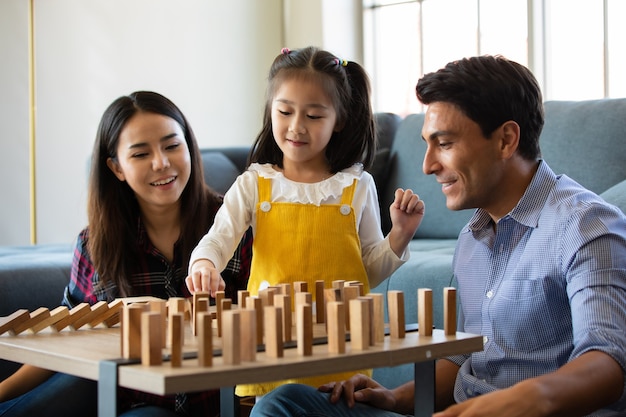 Mix race-familieliefhebbers, blanke vader en aziatische moeder met halfbloed dochter die samen een houten dominospel speelt in de woonkamer met blij en leuk. idee van liefde en relatie, home sweet home.