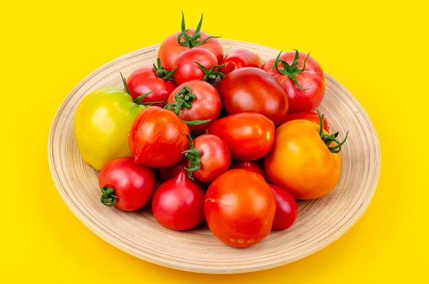 Mix of ripe colorful tomatoes on bright yellow background. Studio Photo.