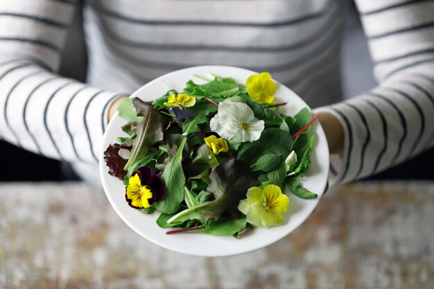 Photo mix of salads with flowers on a white plate held by a girl