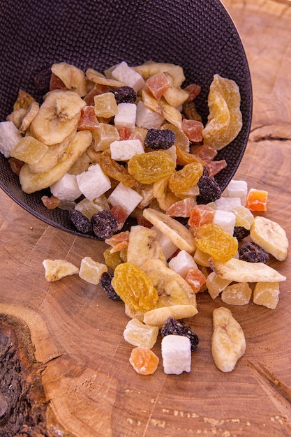 a mix of sliced dried fruits and berries, nuts spilling out of a dark cup on a wooden