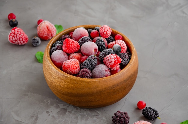 Mix of summer frozen berries in a wooden bowl on a dark