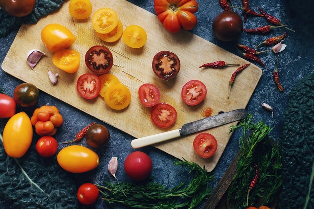 Mix van kleurrijke rauwe verse tomaten en kruiden op donkere stenen tafel en oude houten plank