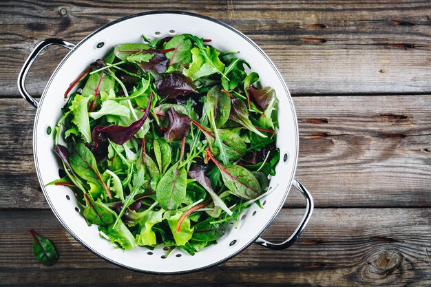 Mix van lente verse bladeren met rucola slabieten Ingrediënten voor salade in vergiet op een rustieke houten achtergrond