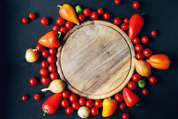 Mix van rauwe verse kerstomaatjes, peper, ui en kruiden op donkere stenen tafel en lege houten plank