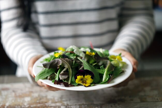 Mix van salades met bloemen op een witte plaat gehouden door een meisje