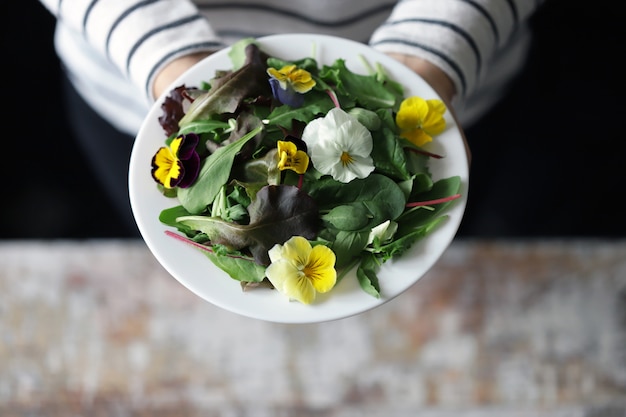 Mix van salades met bloemen op een witte plaat gehouden door een meisje