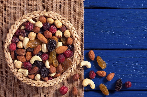 Mix of various nuts and dried fruit in bowl and near on blue wooden table, top view