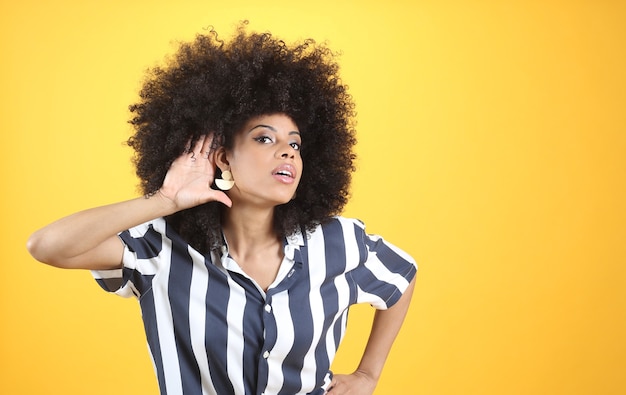 Foto donna afro mista, con problemi di udito, mano sull'orecchio sfondo giallo