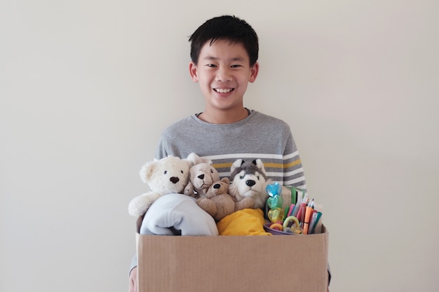 中古のおもちゃでいっぱいの箱を持ってアジアの混合青年ボランティアプレティーン10代の少年