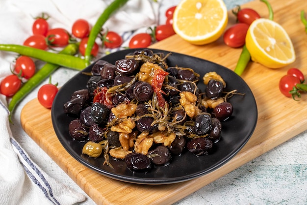 Фото Специальные смешанные оливки, приготовленные с сушеным красным перцем, сушеными на солнце помидорами, тименом, грецкими орехами и розмарином на деревянной тарелке.