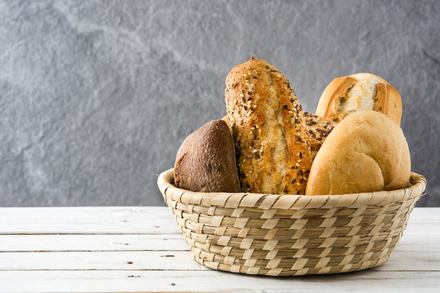 Mixed bread in basket on white wooden table