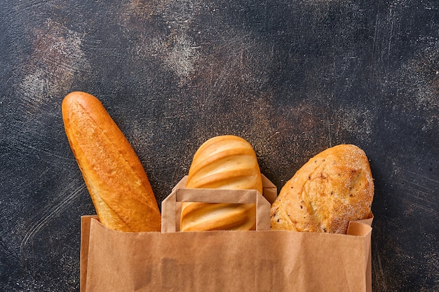 Mixed bread in a paper bag on brown old concrete background table. Top view flat lay with copy space