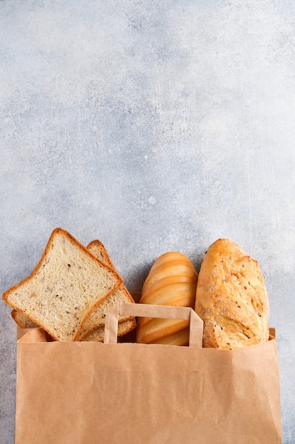 Mixed bread in a paper bag on light gray concrete stone table. Top view with copy space.