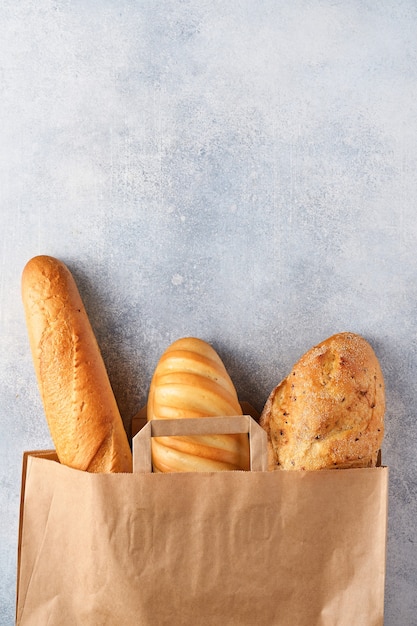 Mixed bread in a paper bag on light gray concrete stone table.